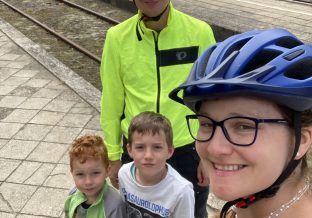 Kobieta z rodziną maż i dwóch synów w kaskach rowerowych na tle torów kolejowych
