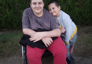 chłopiec na wózku inwalidzkim z młodszym bratem stojącym obok niego