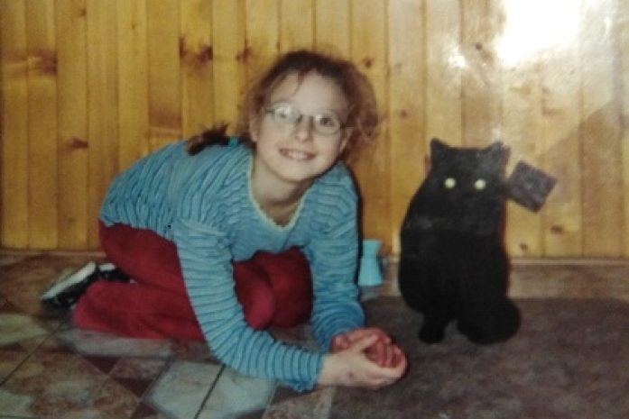 zdjęcie zdjęcia małej dziewczynki w okularach chowającej się pod społem razem z czarnym kotem
